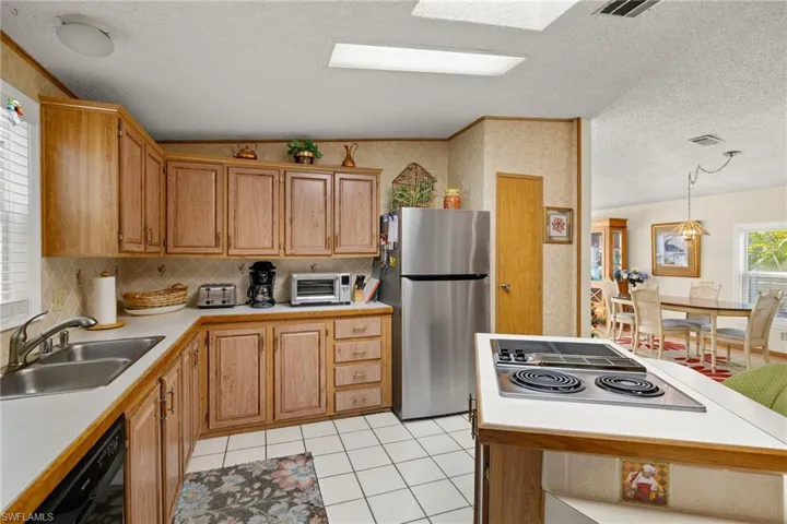 Kitchen featuring sink, hanging light fixtures, a textured ceiling, cooktop, and stainless steel refrigerator
