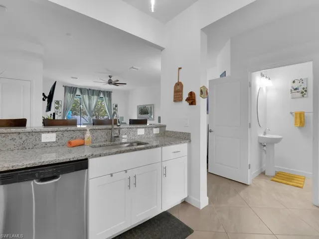 Kitchen with sink, light stone counters, light tile patterned floors, dishwasher, and white cabinets