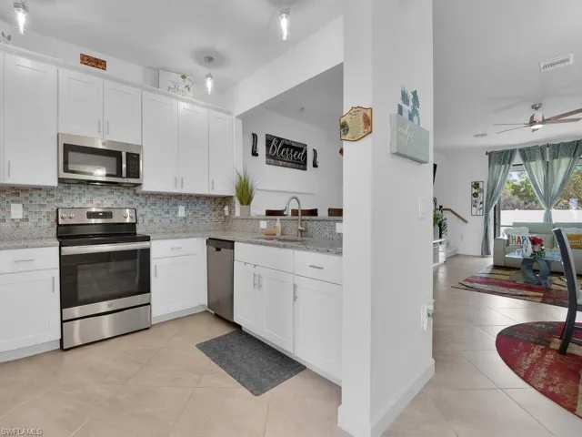 Kitchen featuring sink, white cabinets, backsplash, stainless steel appliances, and light stone countertops
