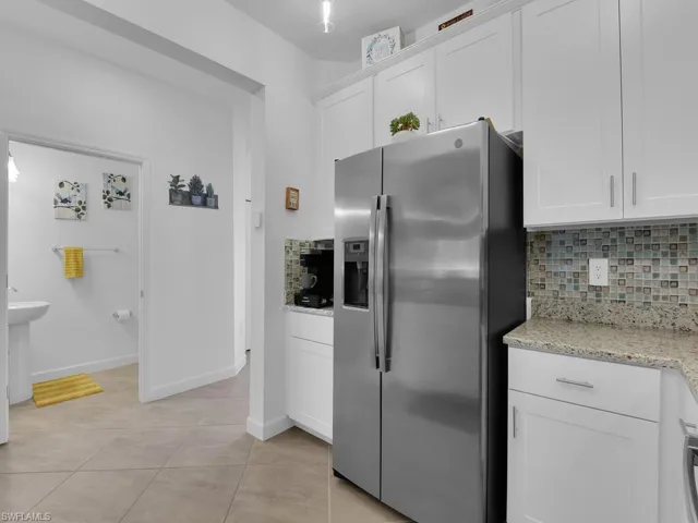 Kitchen featuring stainless steel refrigerator with ice dispenser, white cabinetry, and decorative backsplash
