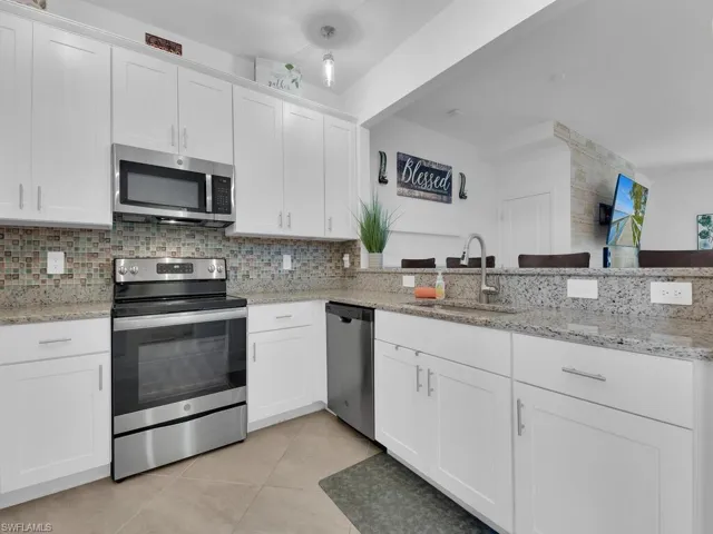 Kitchen featuring sink, light tile patterned floors, white cabinetry, backsplash, and stainless steel appliances