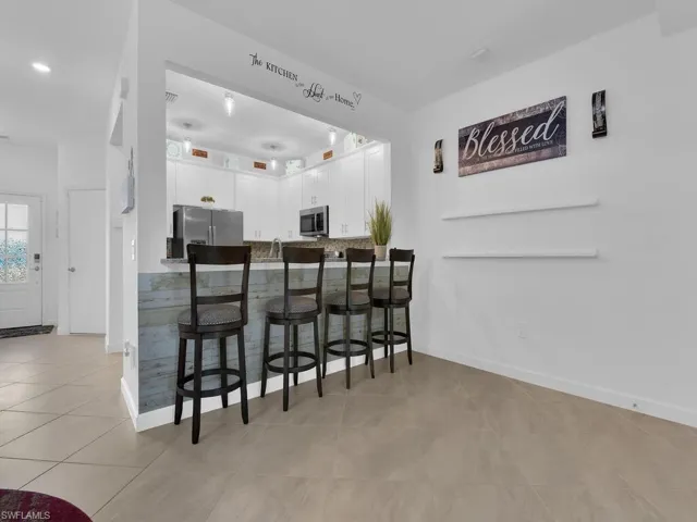 Bar with white cabinetry, appliances with stainless steel finishes, light tile patterned floors, and decorative backsplash