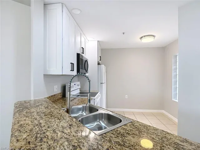 Kitchen featuring white cabinets, white appliances, light tile patterned floors, and dark stone countertops