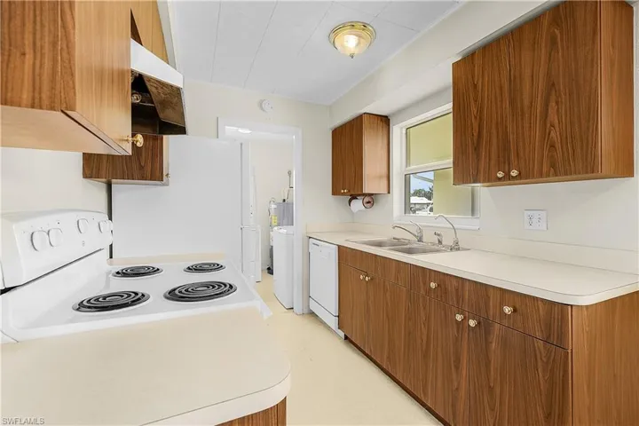Kitchen featuring white appliances, a sink, light countertops, ventilation hood, and brown cabinets