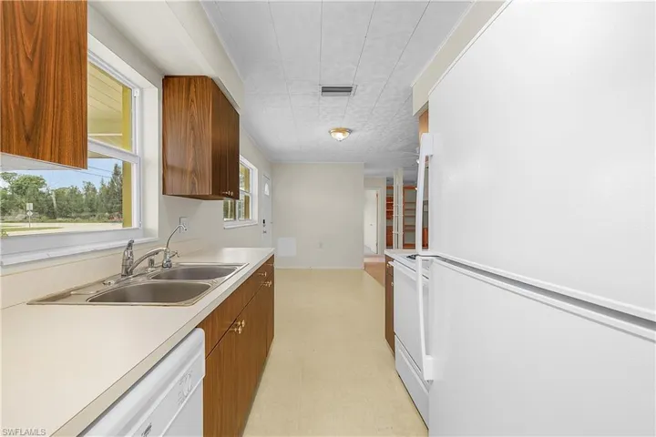 Kitchen with white appliances, brown cabinetry, a sink, and light countertops