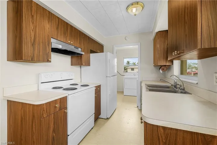 Kitchen featuring under cabinet range hood, white appliances, a sink, and light flooring