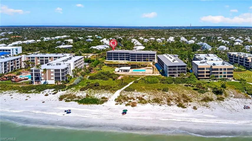Aerial perspective of oceanfront property featuring direct beach access, an outdoor swimming pool, multi-story building structures, and coastal landscaping