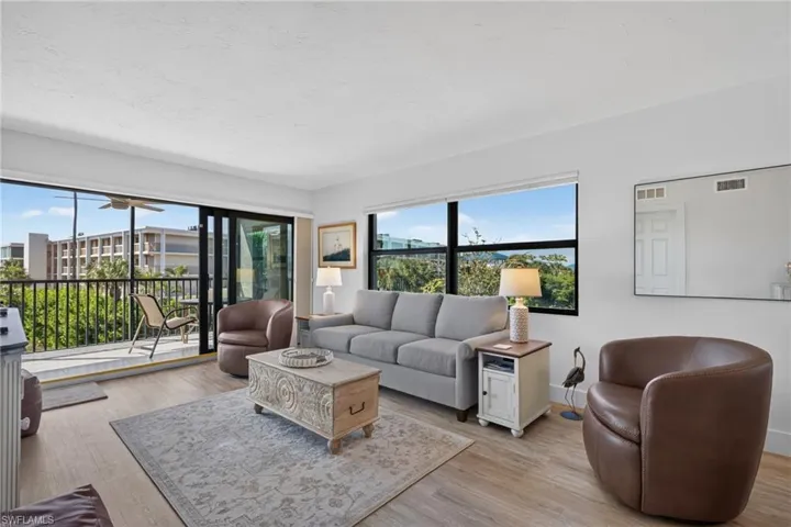 Living area featuring wood-finish flooring, floor-to-ceiling sliding glass doors, large picture windows, and an attached balcony with metal railing