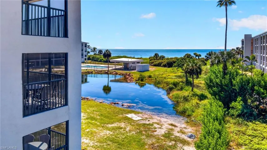 Multi-level screened balconies with black metal railings, overlooking a central water feature, pool area, and coastal horizon