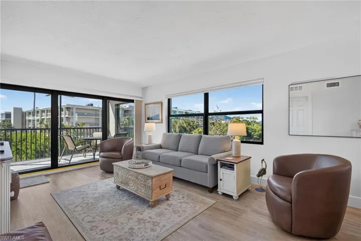 Living area featuring wood-finish flooring, floor-to-ceiling black-frame sliding glass doors, large picture windows, and an attached balcony with black metal railings