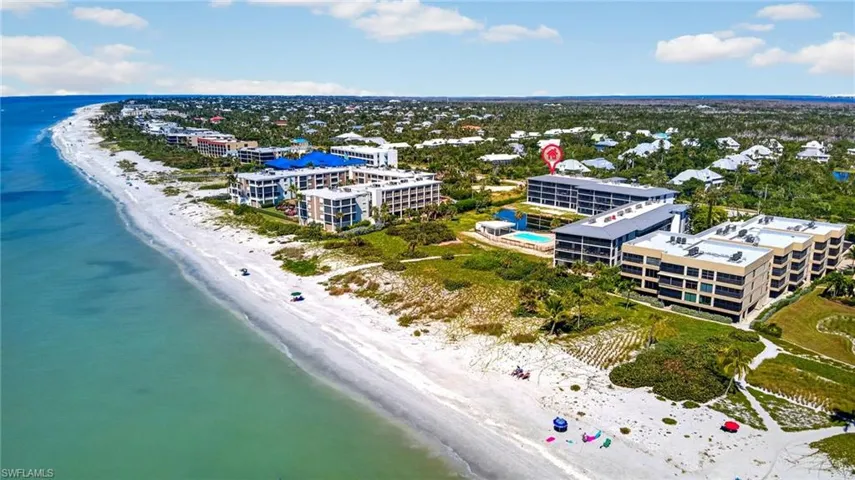 Aerial perspective of multi-story residential complex featuring direct coastal proximity, expansive sand beach, and a swimming pool