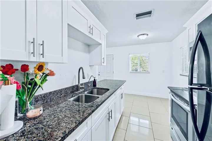 Kitchen featuring appliances with stainless steel finishes, white cabinetry, dark stone counters, light tile patterned flooring, and a textured ceiling