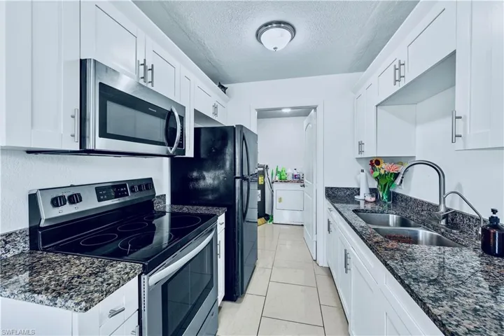Kitchen featuring appliances with stainless steel finishes, a textured ceiling, dark stone counters, white cabinets, and light tile patterned floors