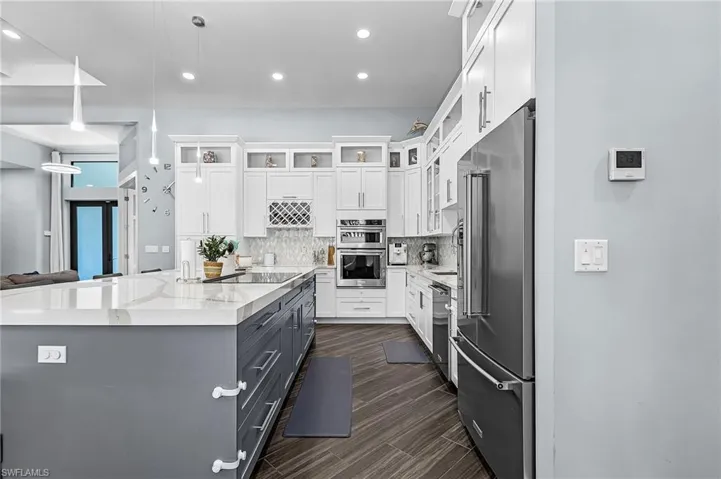 Gourmet kitchen featuring a large central island with a light-toned countertop, stainless steel appliances, white upper cabinetry, gray base cabinetry, and wood-finish flooring