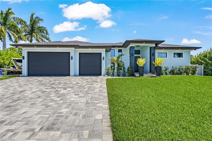 Contemporary exterior featuring a paver driveway, two-car garage, and lush green lawn