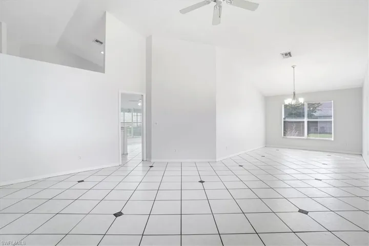 Unfurnished room featuring lofted ceiling, ceiling fan, a chandelier, and light tile patterned floors