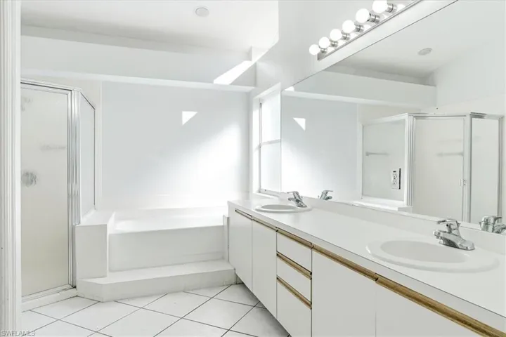 Bathroom featuring double vanity, a garden tub, a shower stall, and light tile patterned floors