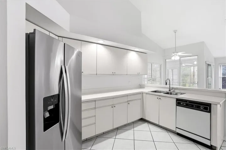 Kitchen featuring light countertops, stainless steel refrigerator with ice dispenser, dishwasher, a peninsula, and vaulted ceiling