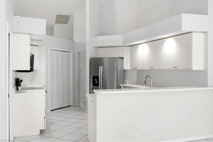 Kitchen with stainless steel fridge with ice dispenser, a peninsula, white cabinetry, light countertops, and a high ceiling