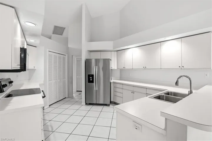 Kitchen with stainless steel fridge with ice dispenser, white range oven, light countertops, a high ceiling, and a peninsula