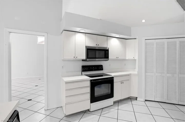 Kitchen featuring range with electric cooktop, light countertops, white cabinetry, stainless steel microwave, and light tile patterned floors