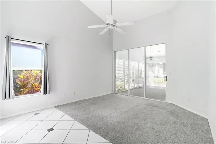 Spare room with a ceiling fan, vaulted ceiling, light colored carpet, light tile patterned floors, and plenty of natural light