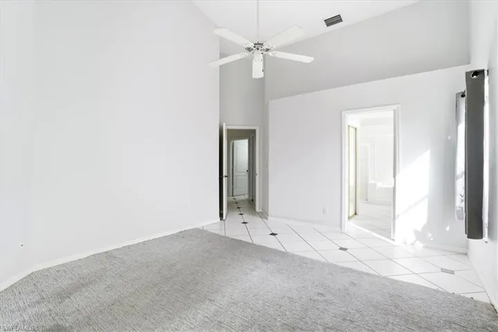 Unfurnished bedroom with light colored carpet, vaulted ceiling, a ceiling fan, and light tile patterned floors