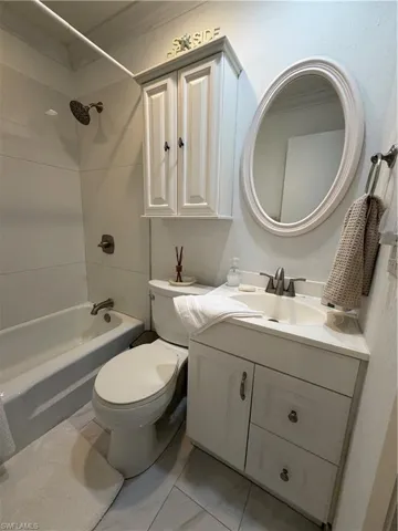 Bathroom featuring a white vanity with cabinet and drawers, an oval mirror, and a built-in tub with a shower fixture