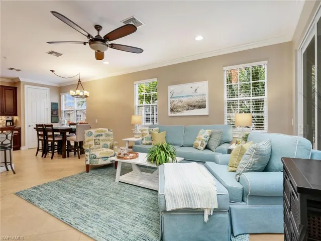 Open Great Room with Crown Molding and Sliders Leading to the Screened In Lanai with Landscaped View, and Eat In Kitchen with Chandelier