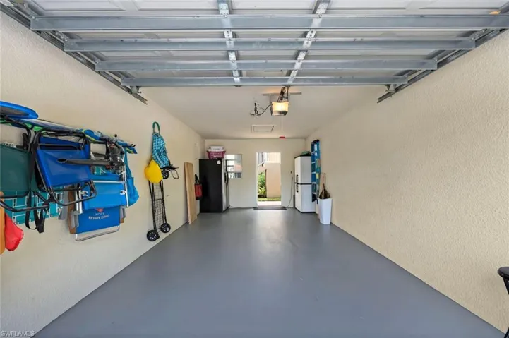 Spacious garage featuring a durable gray floor finish, textured beige walls, exposed overhead garage door track, and an entry door providing exterior access