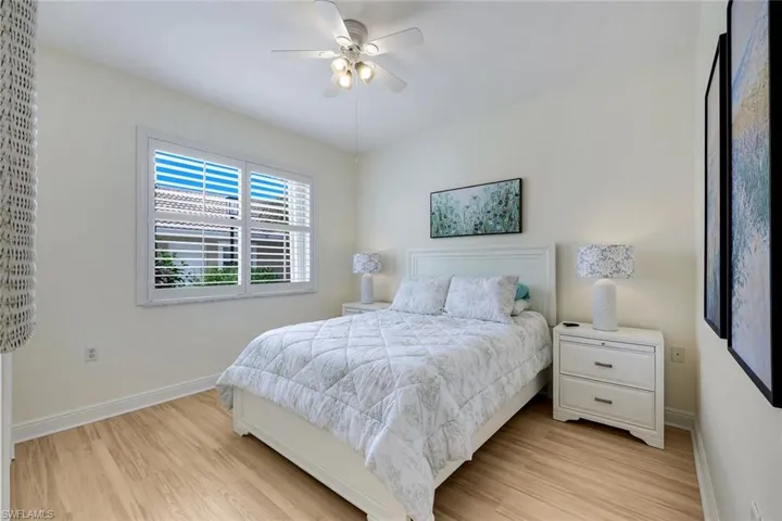 Bedroom featuring wood-finish flooring, white baseboards, and a window with white plantation shutters