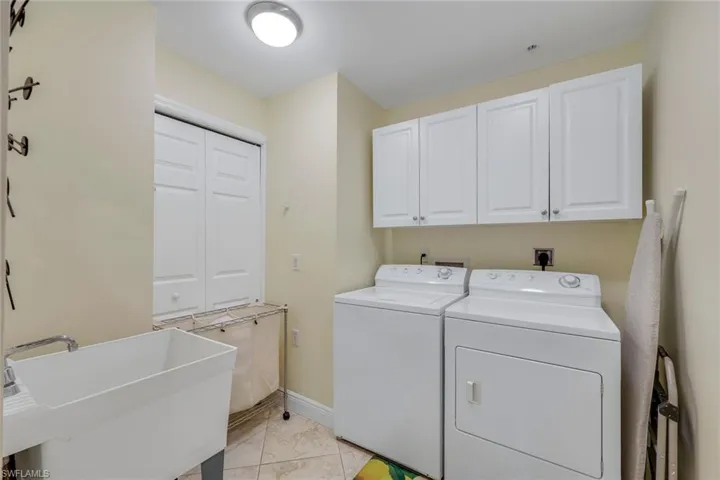 Dedicated laundry area featuring white upper cabinetry, a utility sink with an attached faucet, and tile flooring