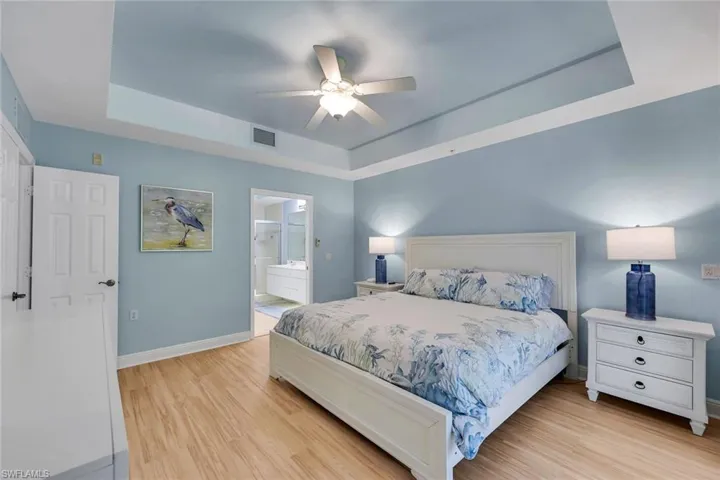 Bedroom featuring a tray ceiling with a ceiling fan, wood-finish flooring, and a private ensuite bathroom