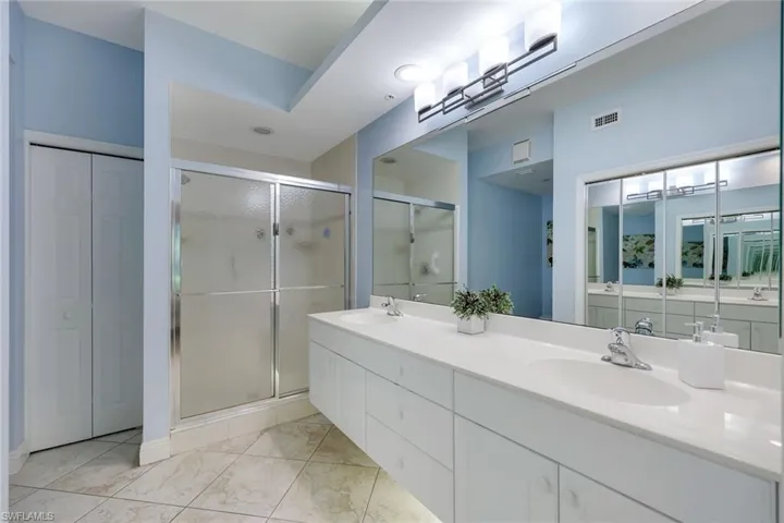 Bathroom featuring a dual vanity with integrated sinks, a large wall-mounted mirror, a shower with frosted glass enclosure, and bi-fold closet doors