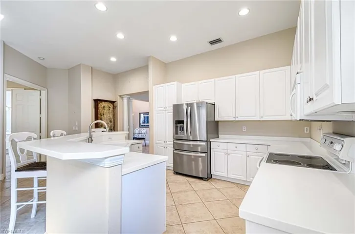 Kitchen featuring white cabinets, light tile patterned floors, white appliances, and a kitchen island with sink