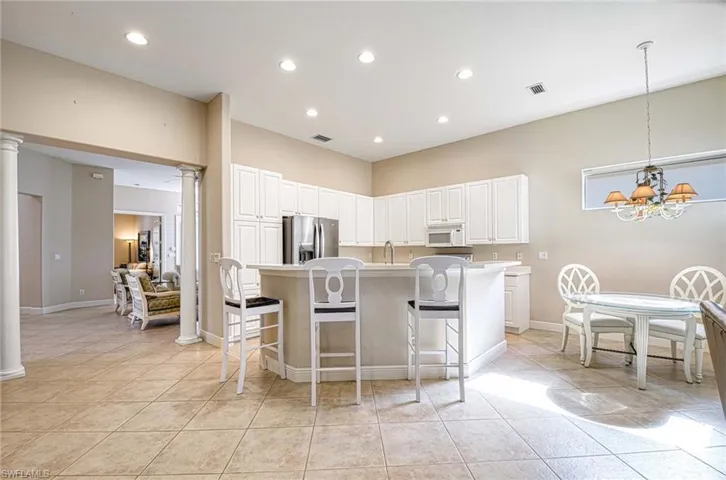Kitchen featuring white cabinets, stainless steel fridge with ice dispenser, an island with sink, and an inviting chandelier