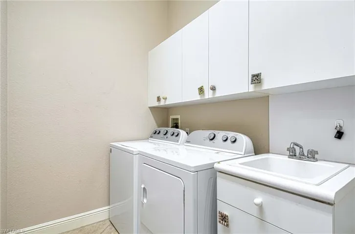 Laundry area featuring sink, light tile patterned floors, cabinets, and independent washer and dryer