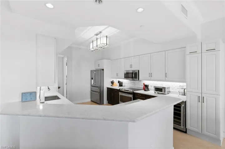 Kitchen with appliances with stainless steel finishes, beverage cooler, tasteful backsplash, white cabinetry, and recessed lighting