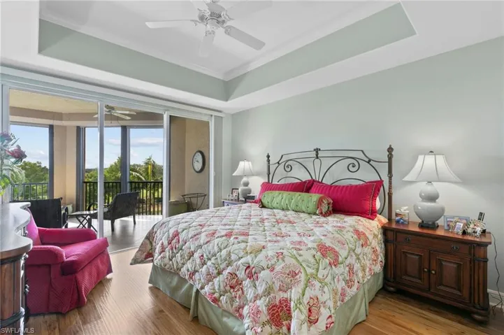 Bedroom featuring access to exterior, wood finished floors, a tray ceiling, a ceiling fan, and ornamental molding