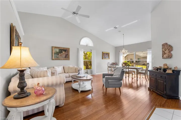 Living room featuring ceiling fan with notable chandelier, wood-type flooring, and lofted ceiling