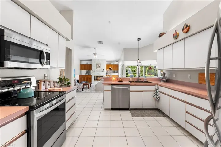 Kitchen with ceiling fan, light tile patterned floors, appliances with stainless steel finishes, decorative light fixtures, and white cabinetry