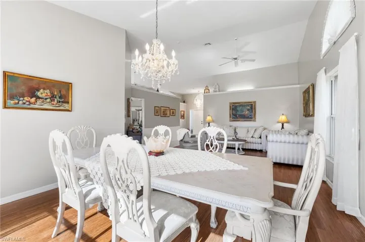 Dining area with vaulted ceiling, dark wood-type flooring, and ceiling fan with notable chandelier