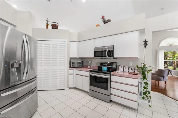 Kitchen featuring white cabinets, high vaulted ceiling, light tile patterned floors, and appliances with stainless steel finishes