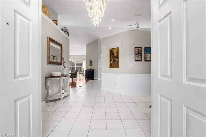Hallway featuring light tile patterned flooring, a chandelier, and ornamental molding