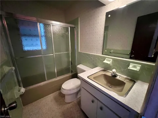 Full bathroom featuring enclosed tub / shower combo, backsplash, toilet, and vanity