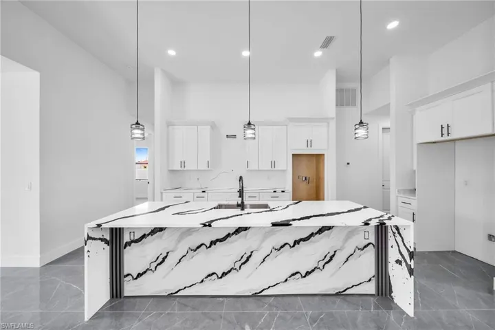 Kitchen with a kitchen island with sink, sink, decorative light fixtures, and white cabinets