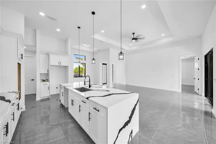 Kitchen with hanging light fixtures, white cabinetry, sink, ceiling fan, and a kitchen island with sink