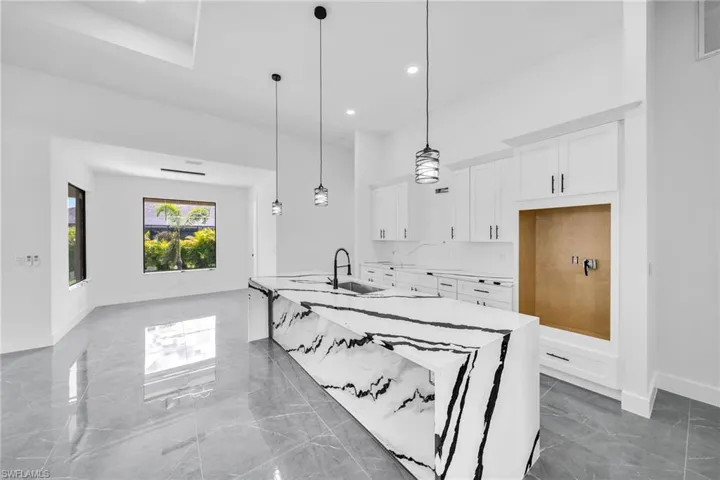 Kitchen with decorative light fixtures, white cabinets, a kitchen island with sink, and sink