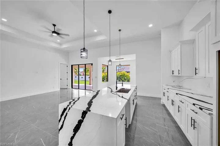 Kitchen featuring light stone countertops, decorative light fixtures, a kitchen island with sink, sink, and ceiling fan