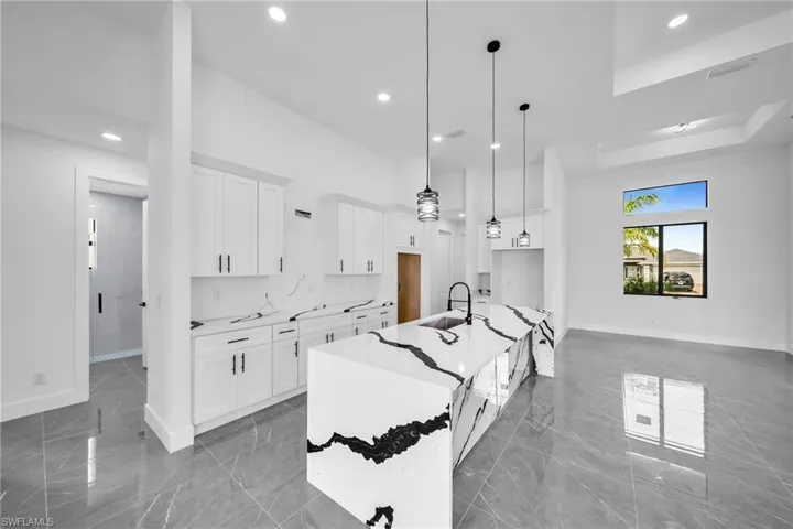 Kitchen with white cabinets, light stone countertops, pendant lighting, and an island with sink